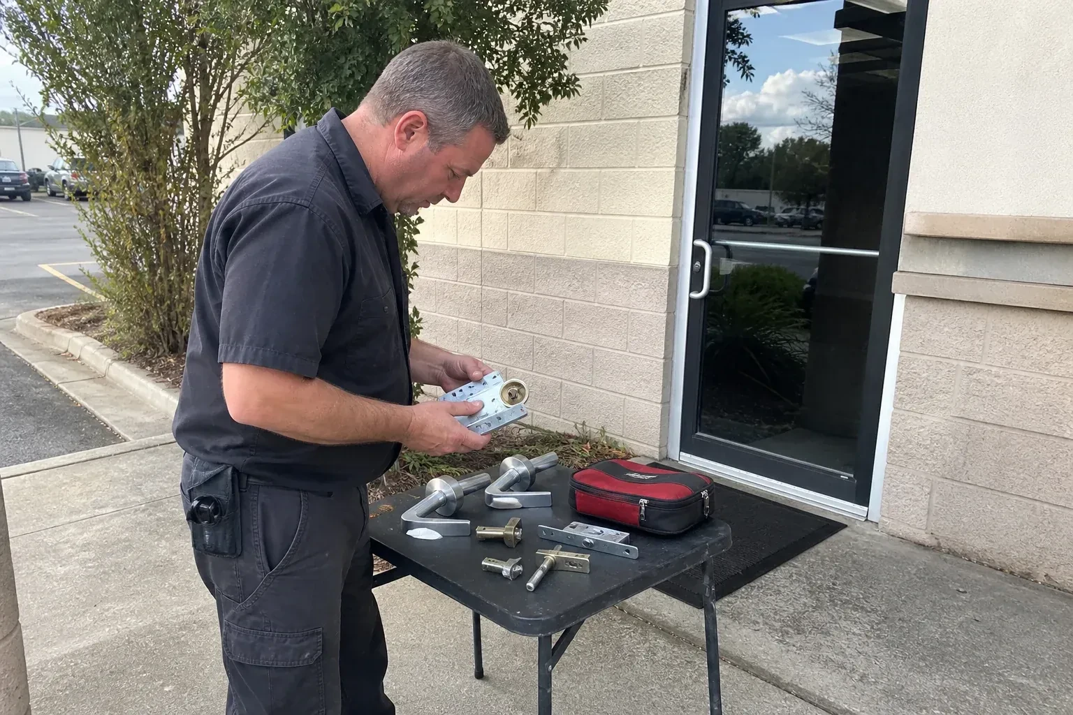 Technician examining detached commercial lock hardware on a table outside a shop entrance. — Business Lockout Service, Toronto